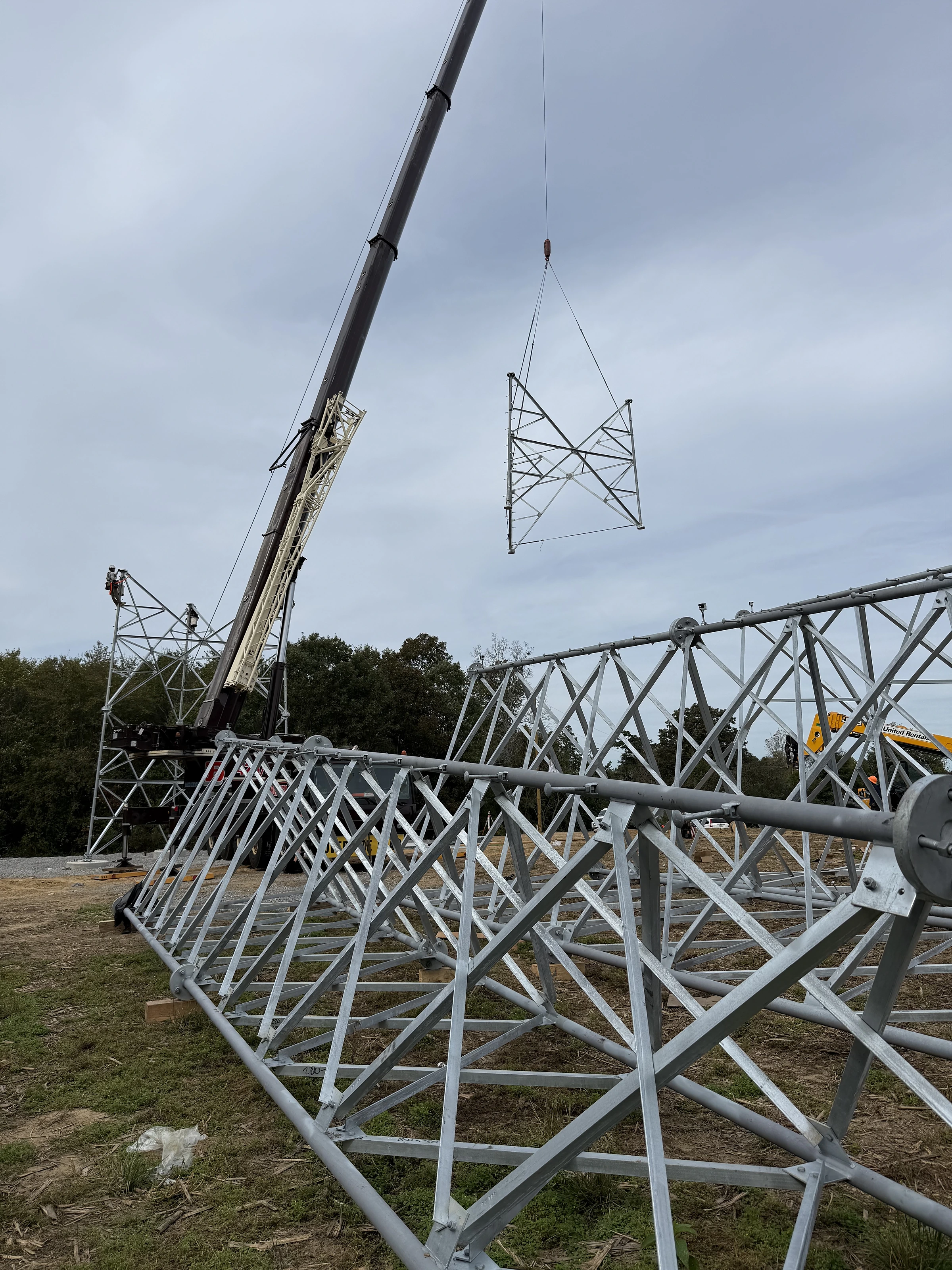Crane lifting a lattice tower section above a tower frame on the ground