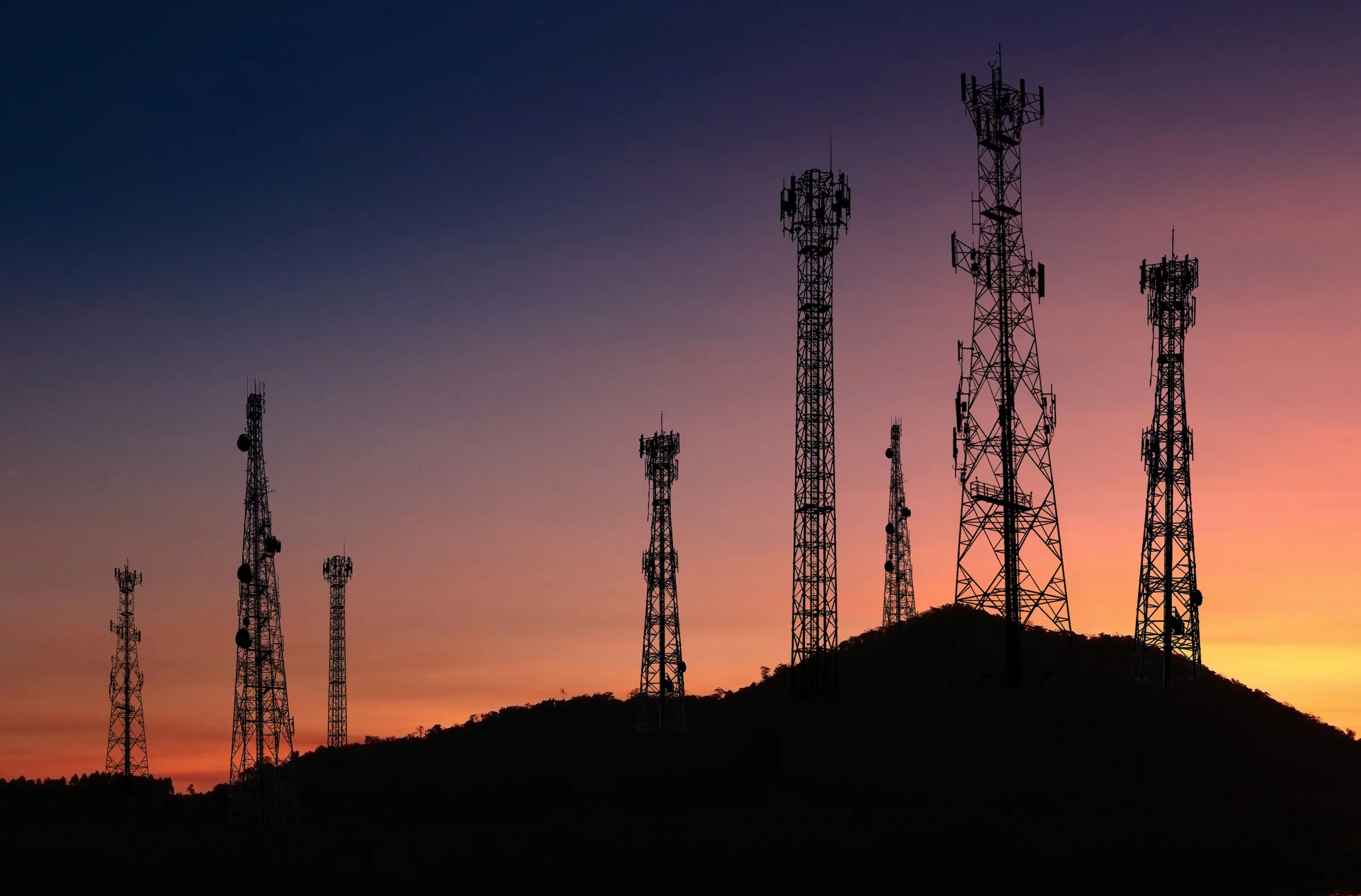Telecommunications towers silhouetted against a sunset sky
